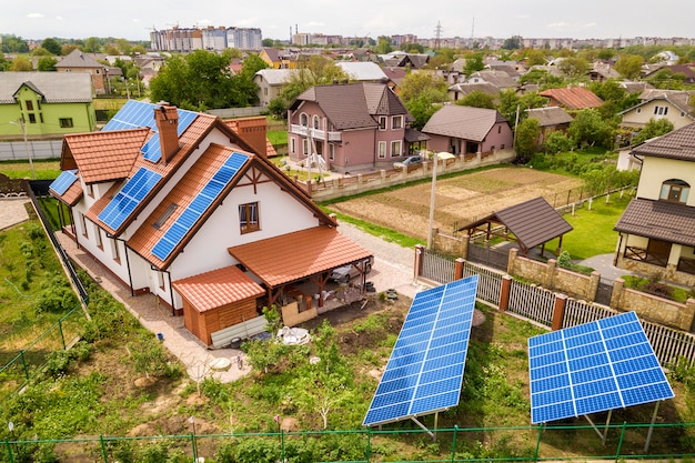 Aerial top view of new modern residential house cottage with blue shiny solar photo voltaic panels system on roof. Renewable ecological green energy production concept.