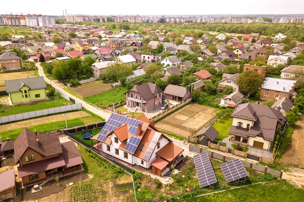 Aerial top view of new modern residential house cottage with blue shiny solar photo voltaic panels system on roof. Renewable ecological green energy production concept.