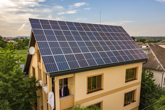 Aerial top view of new modern residential house cottage with blue shiny solar photo voltaic panels system on roof. Renewable ecological green energy production concept.