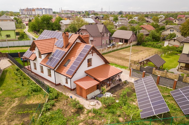 Aerial top view of new modern residential house cottage with blue shiny solar photo voltaic panels system on roof. Renewable ecological green energy production concept.