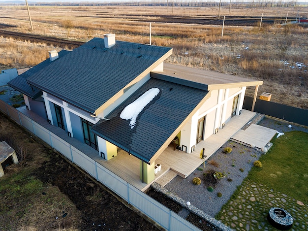 Aerial top view of new residential house cottage and terrace with shingle roof on fenced big yard on sunny winter day.