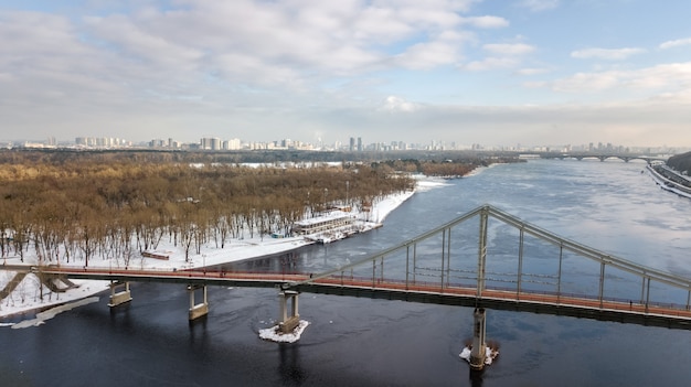 Aerial top view of pedestrian Park bridge in winter and Dnieper river from above, snow Kyiv cityscape, city of Kiev skyline, Ukraine