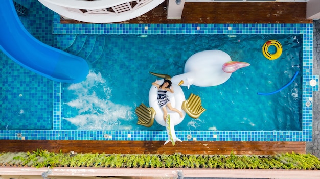 Aerial top view of swimming pool with a woman  relaxing playing on an inflatable mattress in the pool