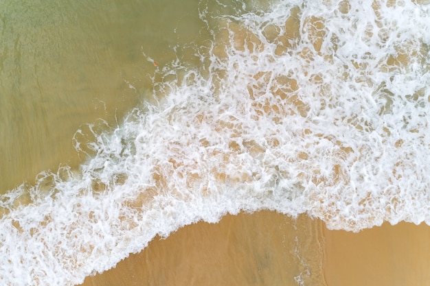 Aerial top view tropical beach sea wave splashing on sandy shore white sea foam.