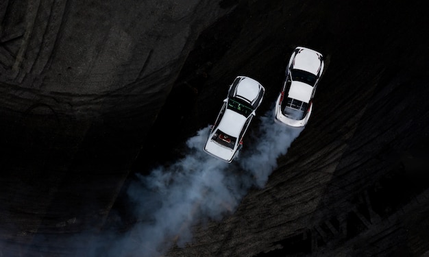 Aerial top view two cars drifting battle on asphalt race track with lots of smoke.