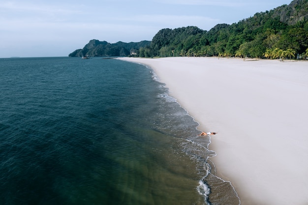 Aerial view: adorable woman in a white swimsuit lying on the sea shore