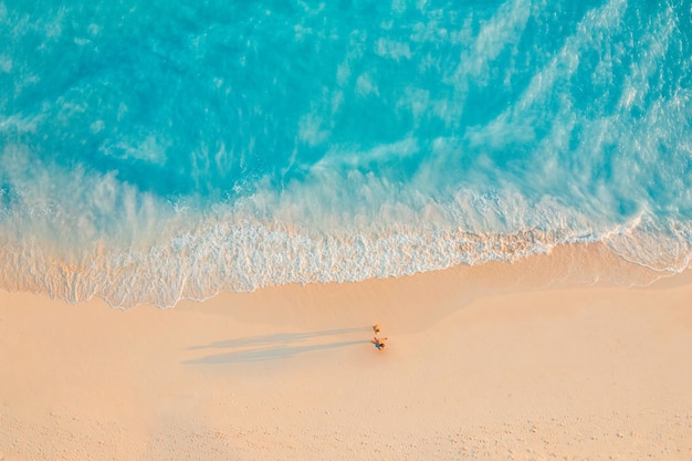 Aerial view of amazing beach with couple walking in sunset light close to turquoise sea. Top view