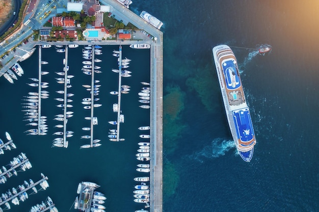 Aerial view of amazing boats and large cruise ship at sunset Minimalistic landscape with boats and sea in marina bay Top view from drone of harbor with yacht motorboat and sailboat Beautiful port