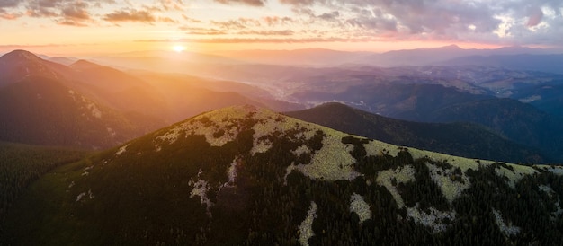 Aerial view of amazing scenery with foggy dark mountain peak covered with forest pine trees at autumn sunrise Beautiful wild woodland with shining rays of light at dawn