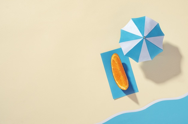 Aerial view of the beach with umbrella and orange slice on a towel on the sand