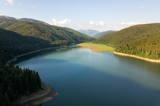 Aerial view of big lake with clear blue water between high mountain hills covered with dense evergreen forest.