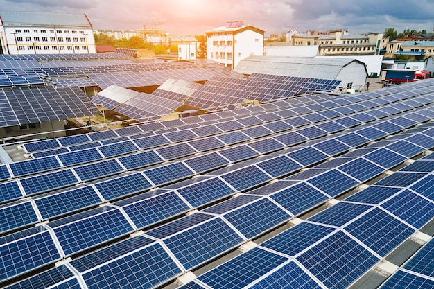 Aerial view of blue photovoltaic solar panels mounted on industrial building roof for producing green ecological electricity. Production of sustainable energy concept.