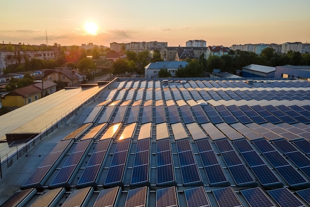 Aerial view of blue photovoltaic solar panels mounted on industrial building roof for producing green ecological electricity at sunset Production of sustainable energy concept