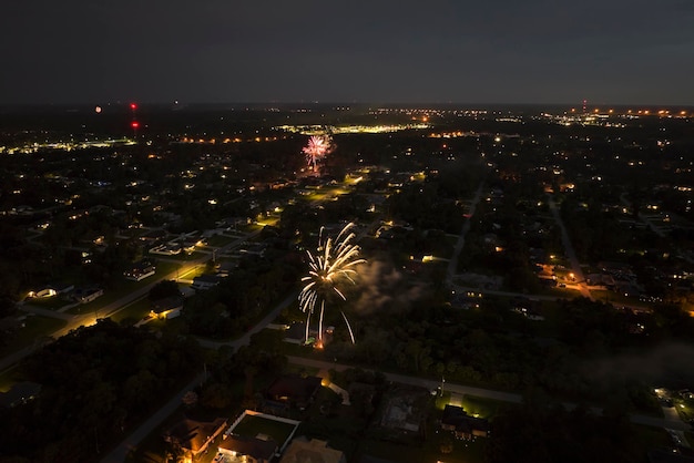 Aerial view of bright fireworks exploding with colorful lights over suburban houses in residential area on US Independence day holiday