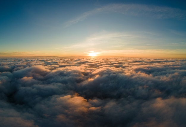 Aerial view of bright yellow sunset over white dense clouds with blue sky overhead.