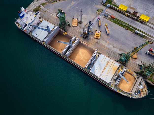 Aerial view of a cargo ship in a harbor uploading grains in a busy port during daylight hours