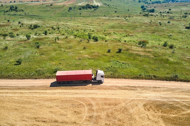 Aerial view of cargo truck driving on dirt road between agricultural wheat fields Transportation of grain after being harvested by combine harvester during harvesting season