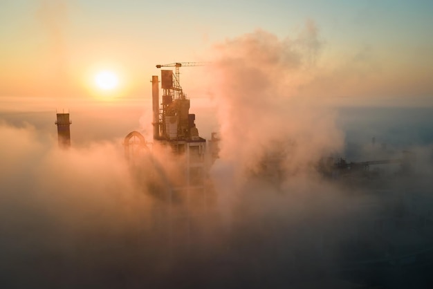 Aerial view of cement factory with high concrete plant structure and tower crane at industrial manufacturing site on foggy evening Production and global industry concept