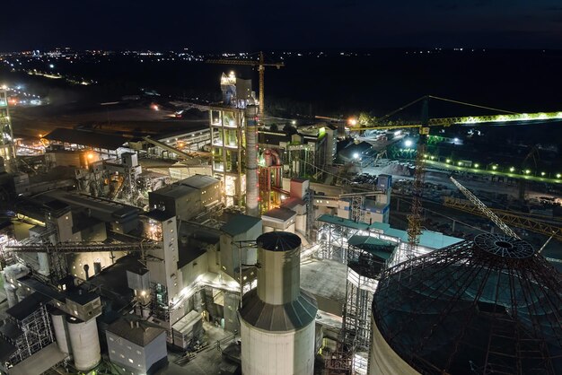 Aerial view of cement factory with high concrete plant structure and tower cranes at industrial production area at night Manufacture and global industry concept