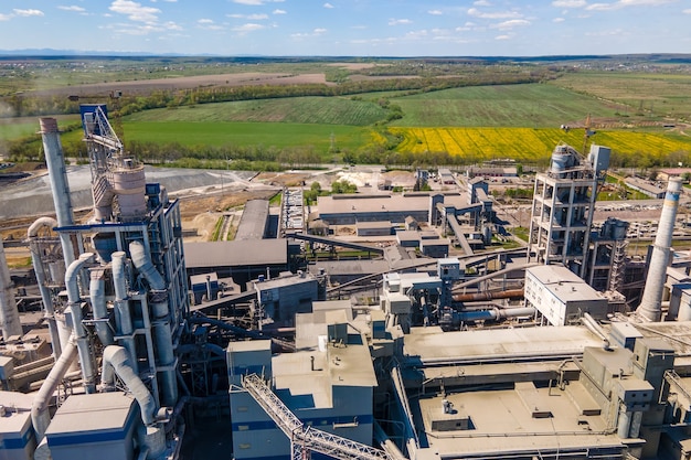 Aerial view of cement plant with high concrete factory structure and tower crane at industrial production area. Manufacture and global industry concept.