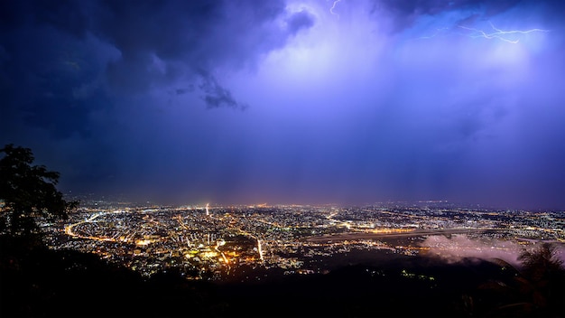 Aerial view City night from the view point on top of mountain in raining storm clouds with lightning Chiang mai Thailand