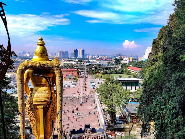 Aerial view of a cityscape covered in greenery with Lord Murugan statue from behind