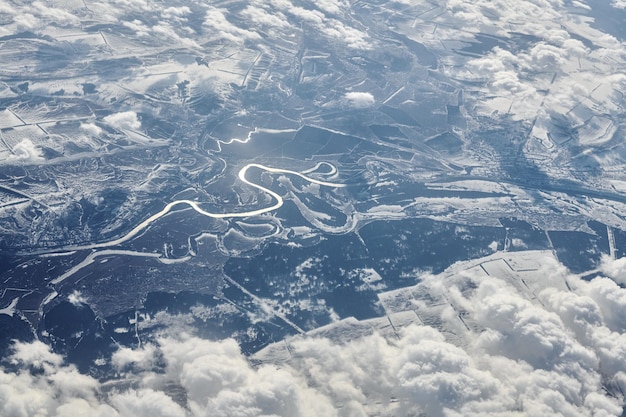 Aerial view over clouds top to snow covered rivers fields and roads winter fresh frosty air