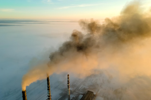 Photo aerial view of coal power plant high pipes with black smoke moving up polluting atmosphere at sunset.