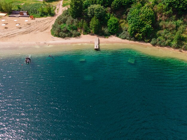 Aerial view of the coast of the lake with the pier, sandy beach and forest 