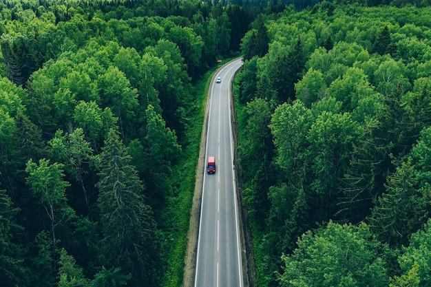 Aerial view of curved country road with cars and truck and green summer woods