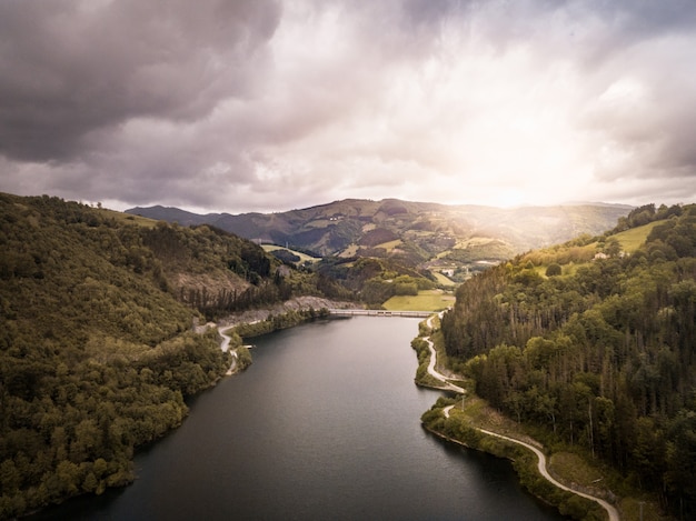 Aerial view of a dam at sunset on a cloudy day in the middle of a mountainous forest. Dam on a mountain river with a road