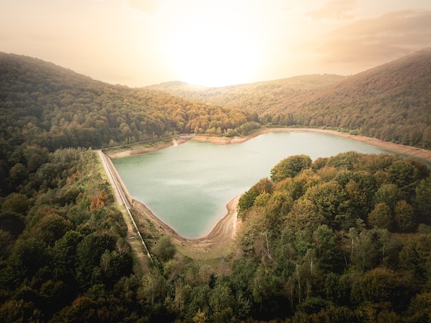 Aerial view of a dam at sunset on a cloudy day in the middle of a mountainous forest. Dam on a mountain river