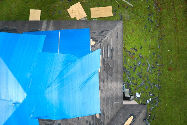 Aerial view of damaged in hurricane Ian house roof covered with blue protective tarp against rain water leaking until replacement of asphalt shingles