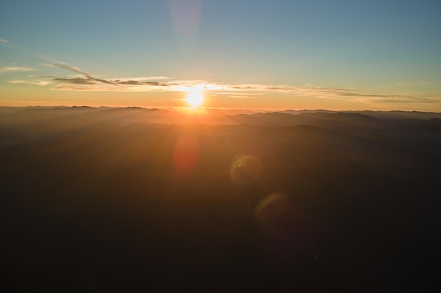 Aerial view of dark mountain hills with bright sunrays of setting sun at sunset Hazy peaks and misty valleys in evening