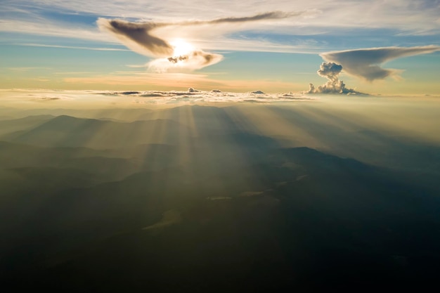 Aerial view of dark mountain hills with bright sunrays of setting sun at sunset Hazy peaks and misty valleys in evening