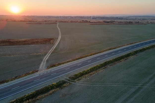 Aerial view of empty intercity road with asphalt surface and white markings in evening