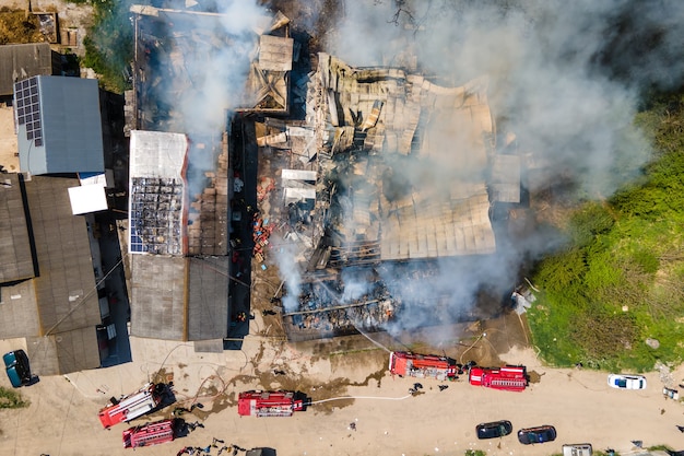 Aerial view of firefighters extinguishing ruined building on fire with collapsed roof and rising dark smoke.