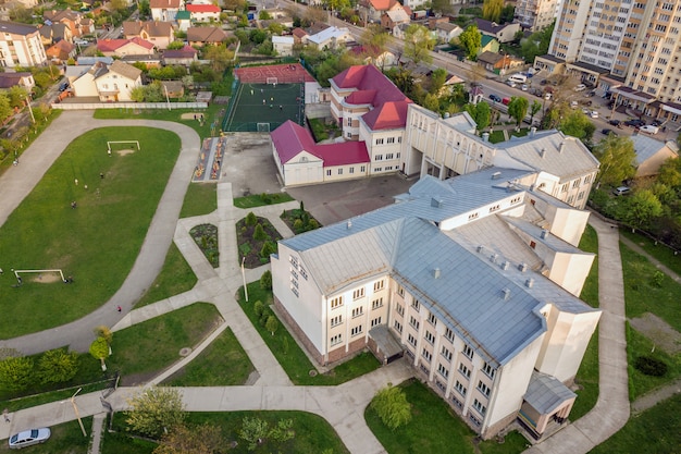 Aerial view of a football field on a stadium covered with green grass and a school building in city area.