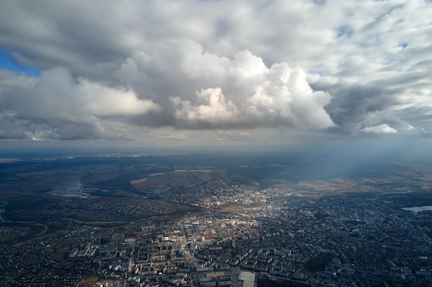 Aerial view from airplane window at high altitude of distant city covered with puffy cumulus clouds forming before rainstorm