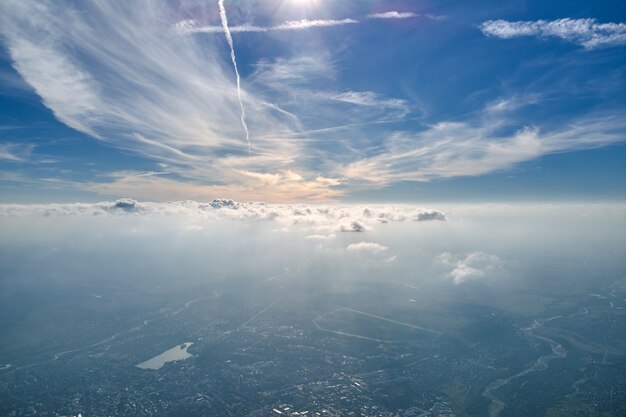 Aerial view from airplane window at high altitude of earth covered with white thin layer of misty haze and distant clouds.