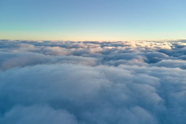 Aerial view from above at high altitude of dense puffy cumulus clouds flying in evening Amazing sunset from airplane window point of view