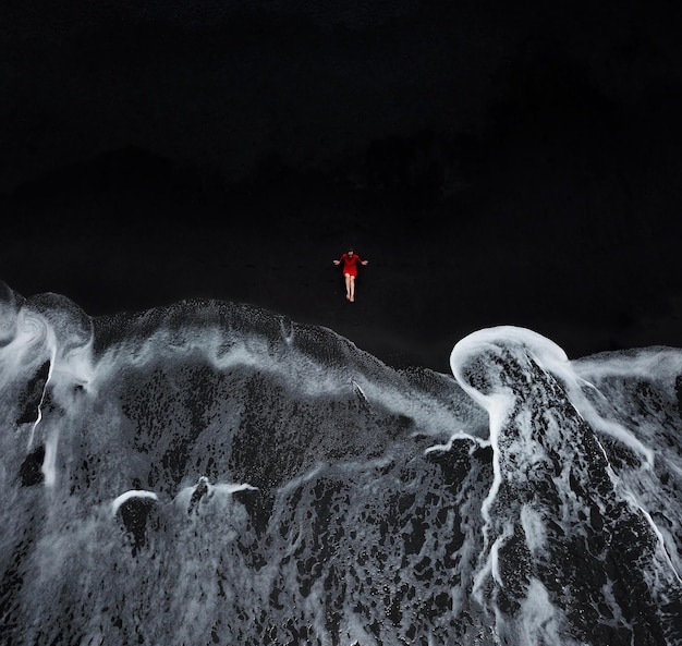 Aerial view of a girl in a red dress sitting on the beach with black sand foaming waves of the Atlantic Ocean Tenerife Canary Islands Spain