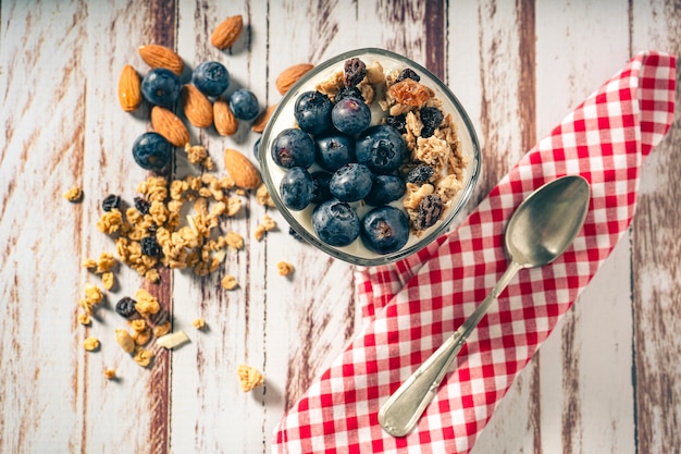 Aerial view of a glass with yogurt, blueberry and granola parfait on a rustic wooden table. Healthy and natural eating concept.