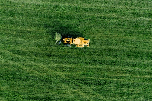 Aerial view of green grass harvest field with tractor moving hay bale in Finalnd