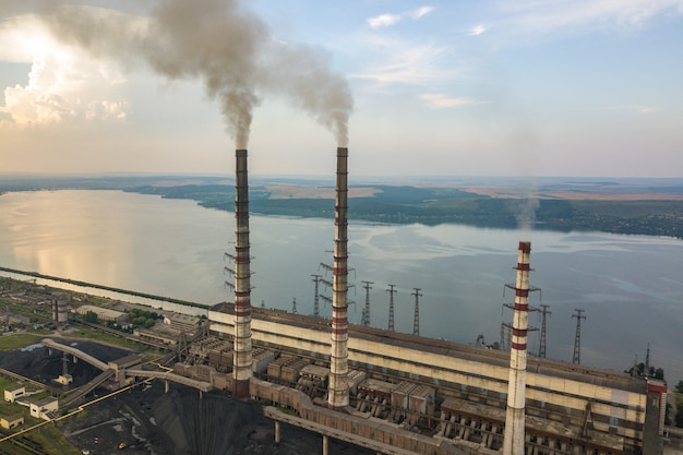 Aerial view of high chimney pipes with grey smoke from coal power plant. Production of electricity with fossil fuel.