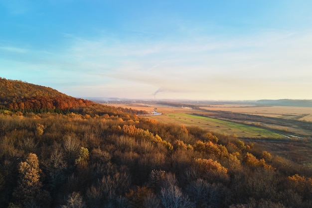 Aerial view of hills covered with dark mixed pine and lush forest with green and yellow trees canopies in autumn mountain woods at sunset Beautiful autumnal evening landscape