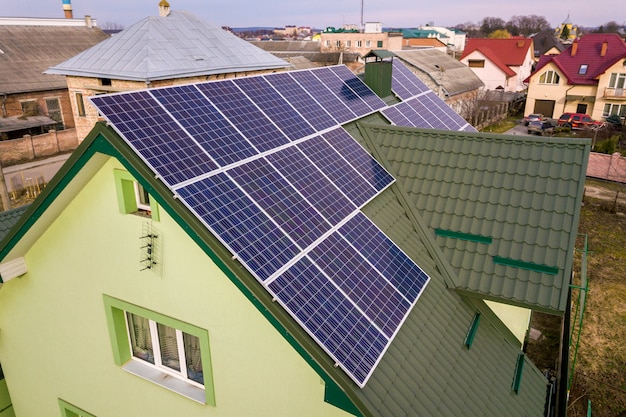 Aerial view of  house cottage with blue shiny solar photo voltaic panels system on the roof.