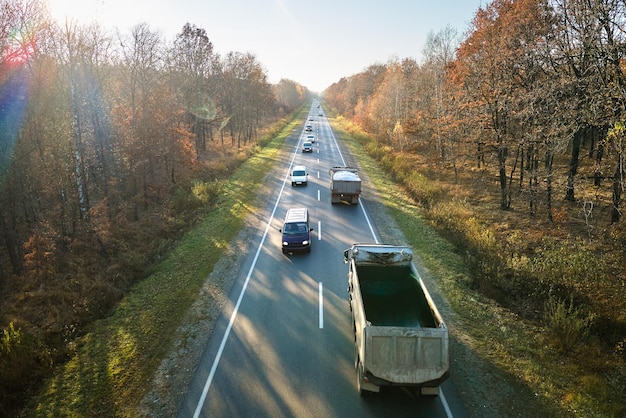 Aerial view of intercity road with fast driving cars between autumn forest trees at sunset. Top view from drone of highway traffic in evening