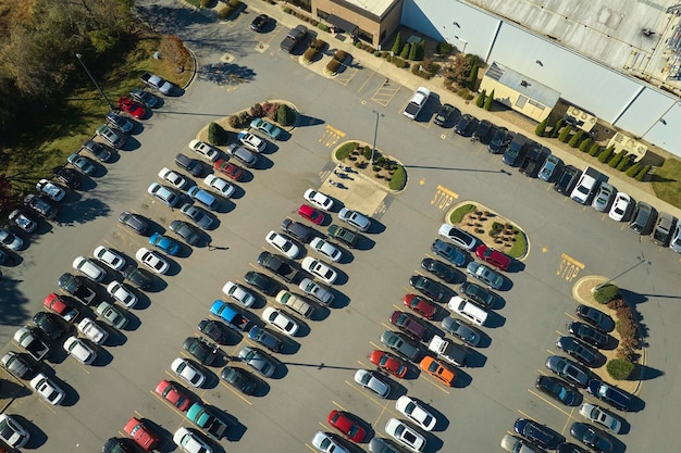 Aerial view of large parking lot in front of rgocery store with many parked colorful cars Carpark at supercenter shopping mall with lines and markings for vehicle places and directions