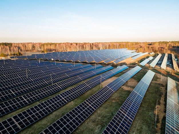 Aerial view of a large solar farm at sunset with rows of photovoltaic panels amidst a natural landscape showcasing renewable energy